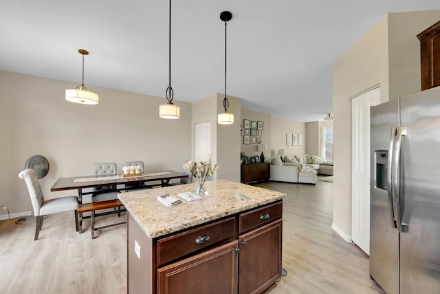 kitchen with light stone counters, stainless steel fridge, a kitchen island, decorative light fixtures, and light hardwood / wood-style flooring