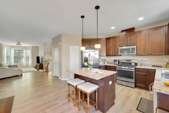 kitchen with light hardwood / wood-style floors, a center island, stainless steel appliances, decorative light fixtures, and light stone countertops