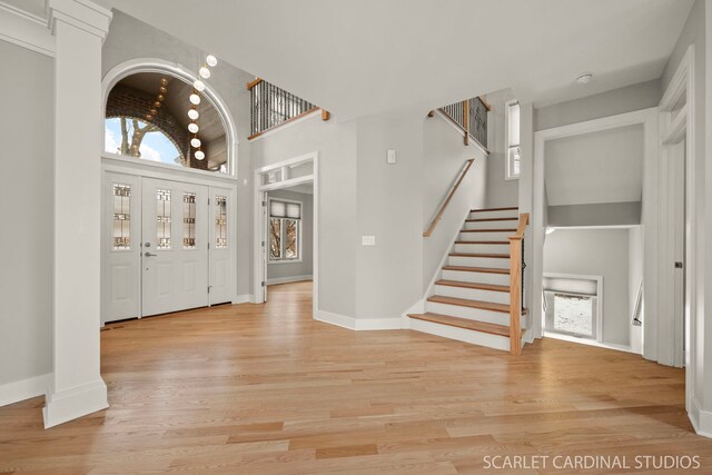 unfurnished living room with a notable chandelier, decorative columns, and light wood-type flooring