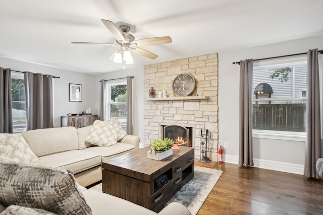 living room with a stone fireplace, dark hardwood / wood-style floors, and ceiling fan