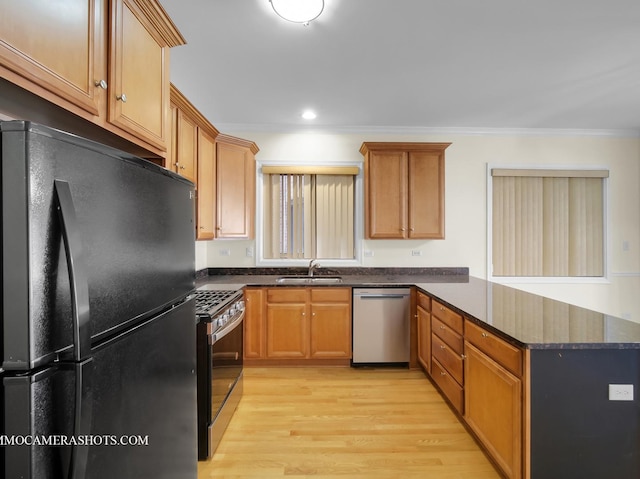 kitchen featuring appliances with stainless steel finishes, dark stone counters, light hardwood / wood-style floors, crown molding, and sink