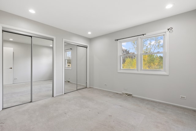 unfurnished bedroom with light carpet and two closets