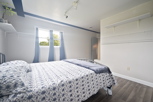 bedroom with rail lighting and dark hardwood / wood-style floors