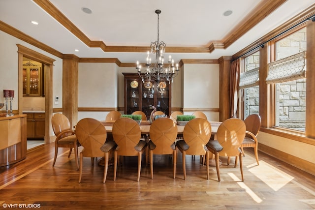 dining space with ornamental molding, hardwood / wood-style flooring, a raised ceiling, and a notable chandelier