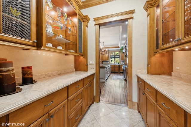 kitchen featuring light stone countertops, light wood-type flooring, a chandelier, and ornamental molding