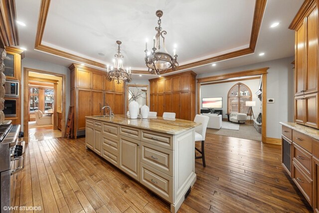 kitchen featuring a raised ceiling, a center island with sink, dark hardwood / wood-style floors, a notable chandelier, and a breakfast bar area