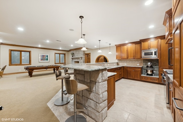 kitchen featuring a breakfast bar, pool table, light stone counters, appliances with stainless steel finishes, and decorative light fixtures