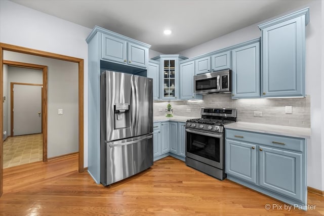 kitchen with decorative backsplash, stainless steel appliances, blue cabinets, and light wood-type flooring