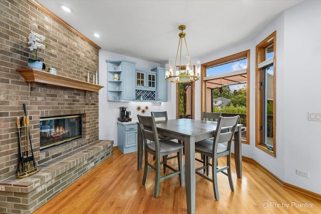 dining room with light wood-type flooring, a chandelier, and a brick fireplace