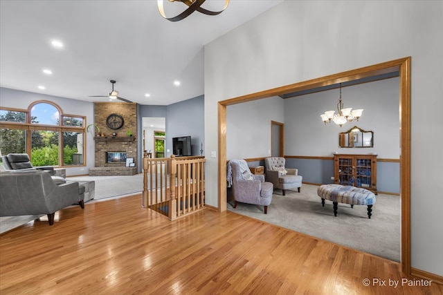 living room with ceiling fan with notable chandelier, a fireplace, lofted ceiling, and light hardwood / wood-style flooring