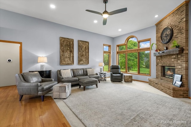 living room with a brick fireplace, ceiling fan, and wood-type flooring