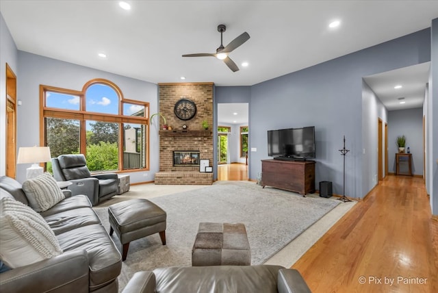 living room featuring a brick fireplace, light wood-type flooring, and ceiling fan