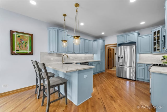 kitchen with light hardwood / wood-style floors, kitchen peninsula, stainless steel appliances, decorative light fixtures, and blue cabinetry