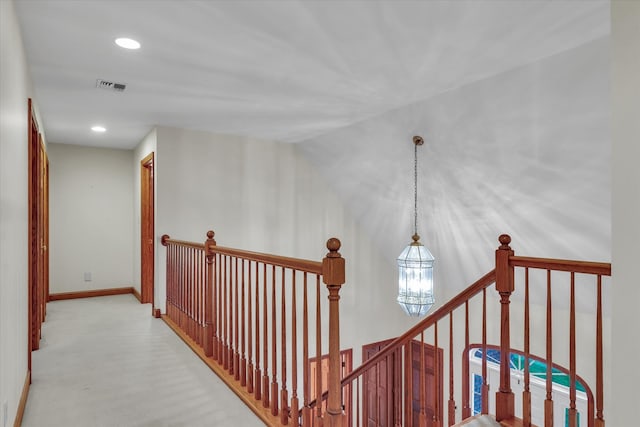 hallway featuring an inviting chandelier and light colored carpet