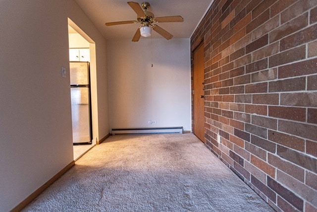 carpeted spare room with ceiling fan, brick wall, and a baseboard heating unit