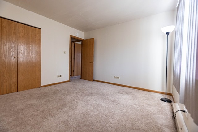 unfurnished bedroom featuring light carpet, a baseboard heating unit, and a closet