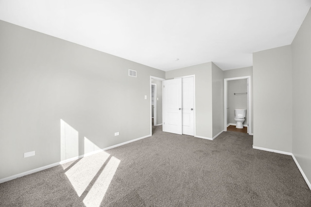 unfurnished bedroom with a closet, ensuite bath, and dark colored carpet