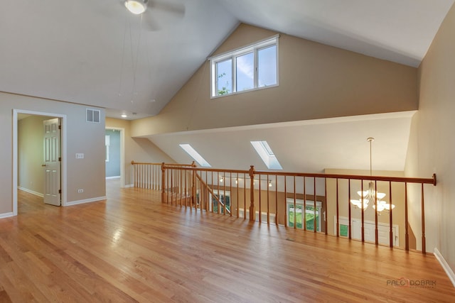 interior space featuring light wood-type flooring, ceiling fan with notable chandelier, a skylight, and high vaulted ceiling