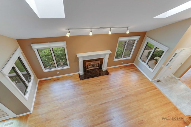 unfurnished living room featuring a skylight, light hardwood / wood-style floors, a high end fireplace, and rail lighting