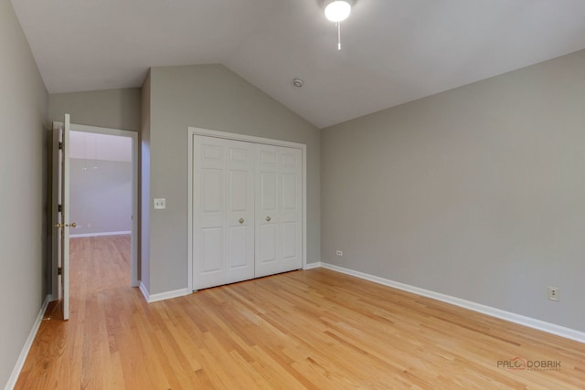 unfurnished bedroom with light wood-type flooring, vaulted ceiling, and a closet