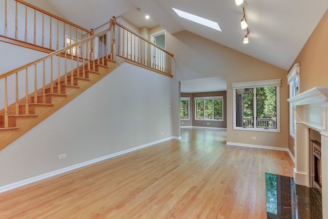 unfurnished living room with high vaulted ceiling, a skylight, track lighting, and hardwood / wood-style flooring