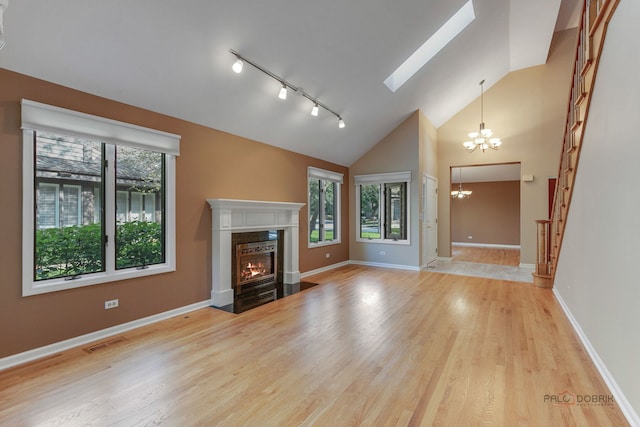 unfurnished living room with a chandelier, track lighting, a fireplace, light hardwood / wood-style flooring, and high vaulted ceiling