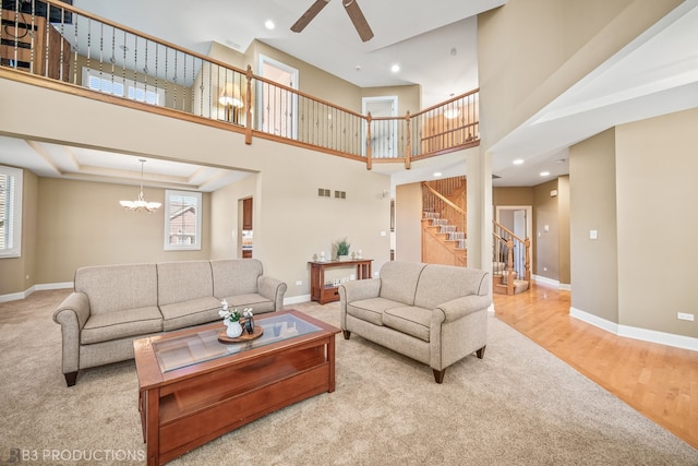 living room with a healthy amount of sunlight, light hardwood / wood-style floors, ceiling fan with notable chandelier, and a towering ceiling