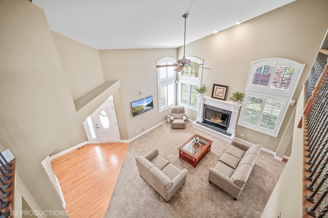 living room featuring light wood-type flooring, a fireplace, a towering ceiling, and ceiling fan