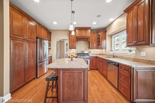 kitchen with hanging light fixtures, sink, stainless steel appliances, a center island, and light hardwood / wood-style floors