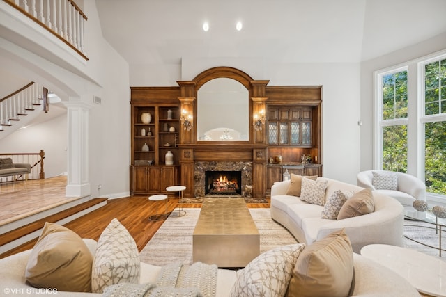 living room with a towering ceiling, hardwood / wood-style flooring, decorative columns, and a premium fireplace