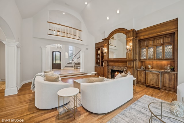 living room with decorative columns, light hardwood / wood-style flooring, a fireplace, and high vaulted ceiling