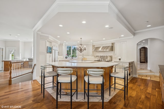 kitchen with wall chimney exhaust hood, dark hardwood / wood-style floors, and a large island with sink