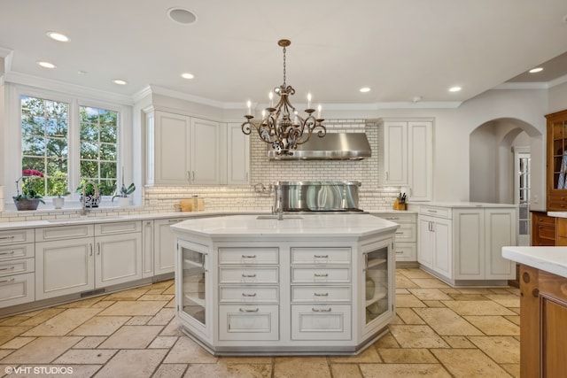 kitchen featuring backsplash, wall chimney exhaust hood, decorative light fixtures, and a kitchen island