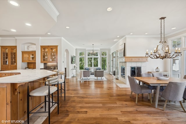 dining area with light hardwood / wood-style floors, crown molding, a notable chandelier, and a tile fireplace