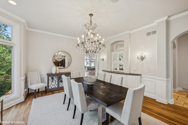 dining area with light hardwood / wood-style flooring, ornamental molding, and a notable chandelier