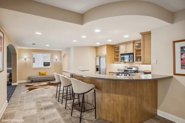 kitchen with light brown cabinetry, a breakfast bar, kitchen peninsula, and stainless steel appliances