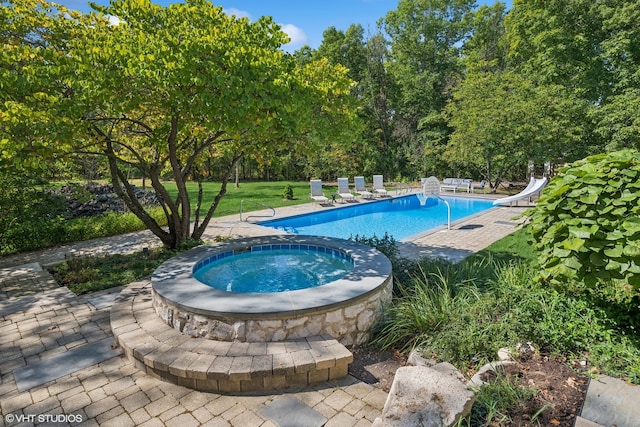 view of pool with an in ground hot tub, a patio area, a water slide, and a yard