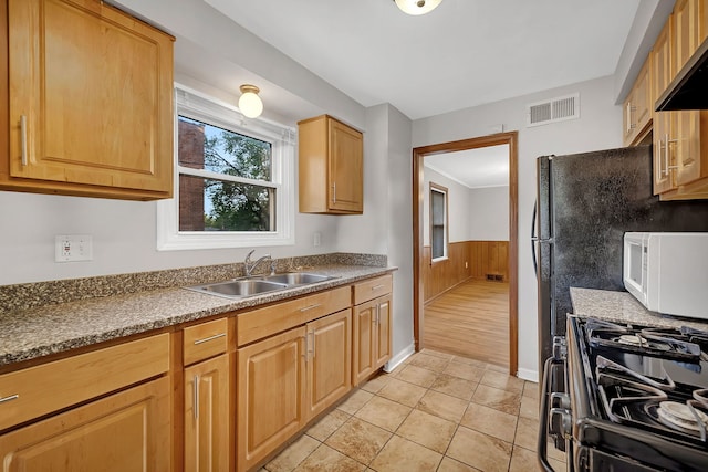 kitchen featuring wood walls, light tile patterned floors, sink, stainless steel gas range, and ventilation hood