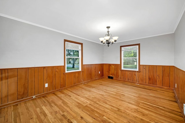 spare room with wood walls, ornamental molding, light hardwood / wood-style flooring, and a notable chandelier