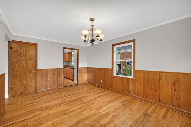 spare room featuring light wood-type flooring, wood walls, ornamental molding, and a chandelier