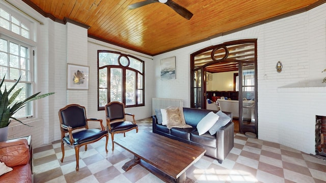 sitting room with wood ceiling, ornamental molding, ceiling fan, and brick wall