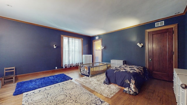 bedroom with crown molding, radiator heating unit, and light wood-type flooring