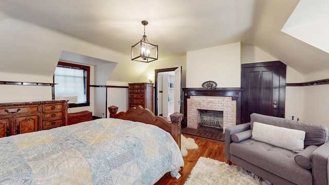 bedroom featuring lofted ceiling, a fireplace, a chandelier, and wood-type flooring