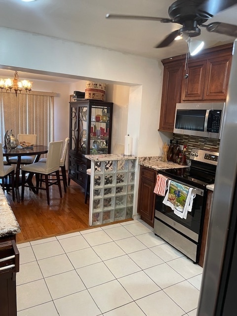 kitchen with light wood-type flooring, light stone counters, tasteful backsplash, ceiling fan with notable chandelier, and stainless steel appliances