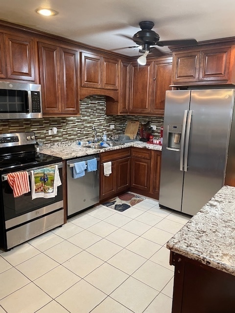 kitchen featuring appliances with stainless steel finishes, tasteful backsplash, light stone countertops, ceiling fan, and sink