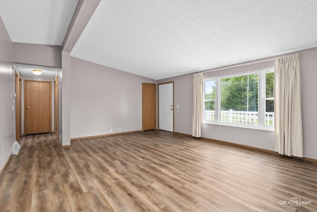 unfurnished room with wood-type flooring, a textured ceiling, and vaulted ceiling