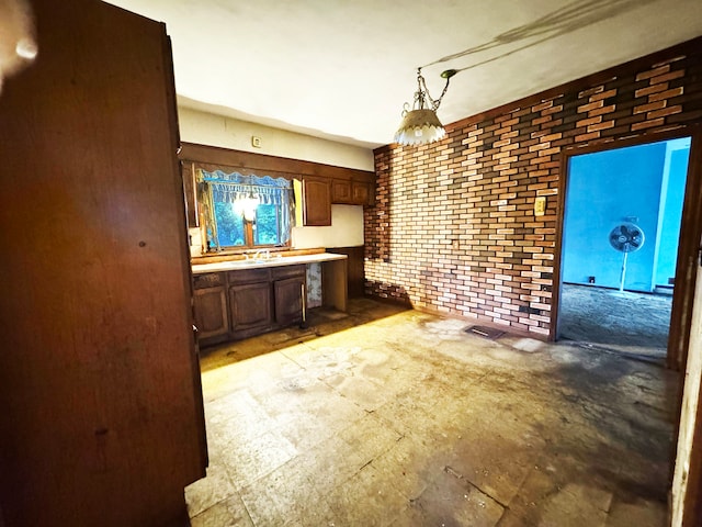 kitchen featuring pendant lighting, dark brown cabinets, and brick wall