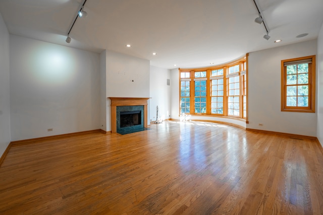 unfurnished living room with light wood-type flooring, a premium fireplace, and track lighting