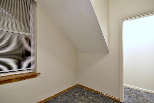 bonus room with vaulted ceiling, dark colored carpet, and baseboards