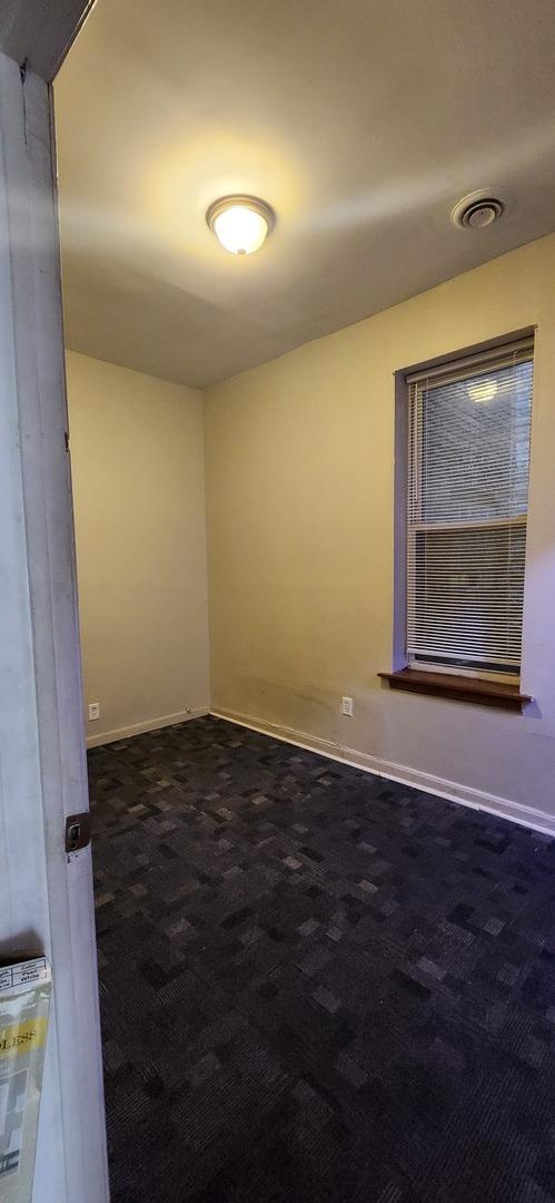 spare room featuring dark colored carpet, visible vents, and baseboards